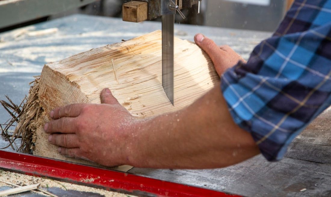 man holding a block of wood with two hands while a bandsaw blade cuts through it
