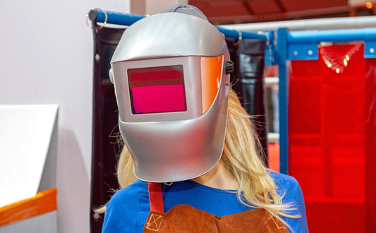 Female welder wearing silver auto-darkening welding helmet in shop