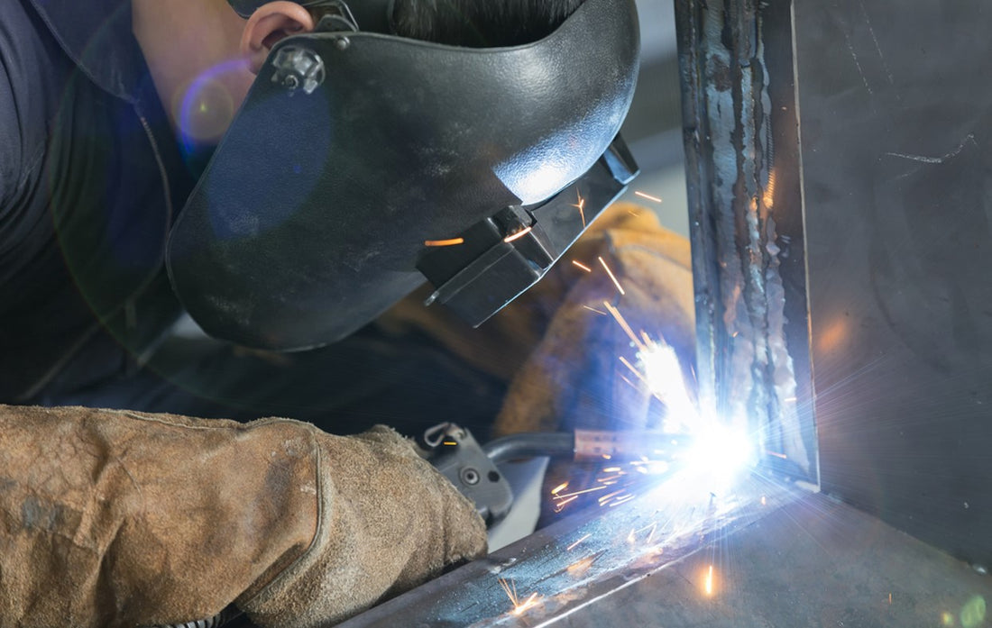 Man in welding helmet and gloves welding steel with MIG wire