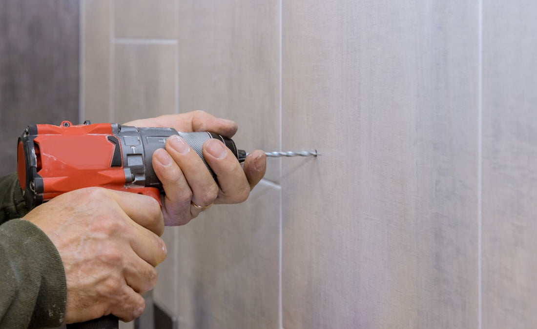 Man using electric drill to drill into porcelain tile on wall