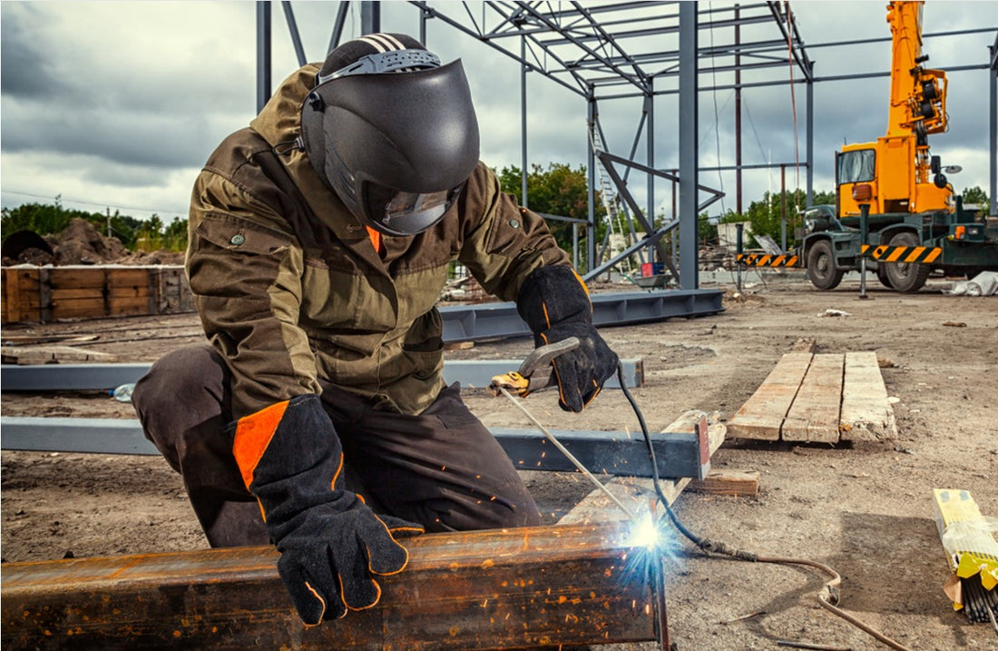 Man welding large square pipe on ground of construction site
