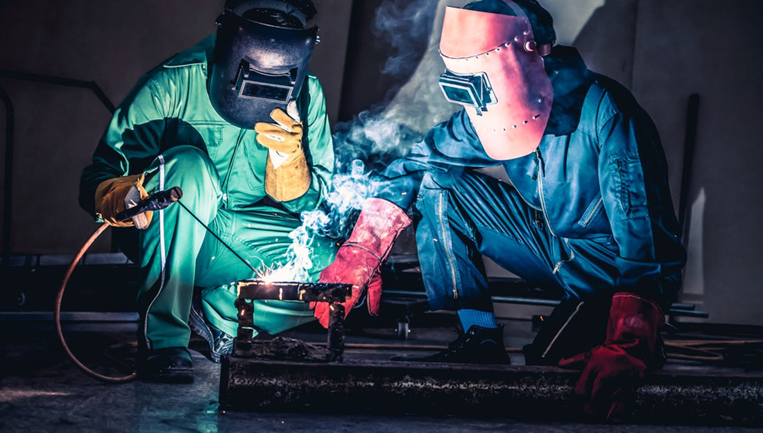 Two welders in protective equipment welding steel