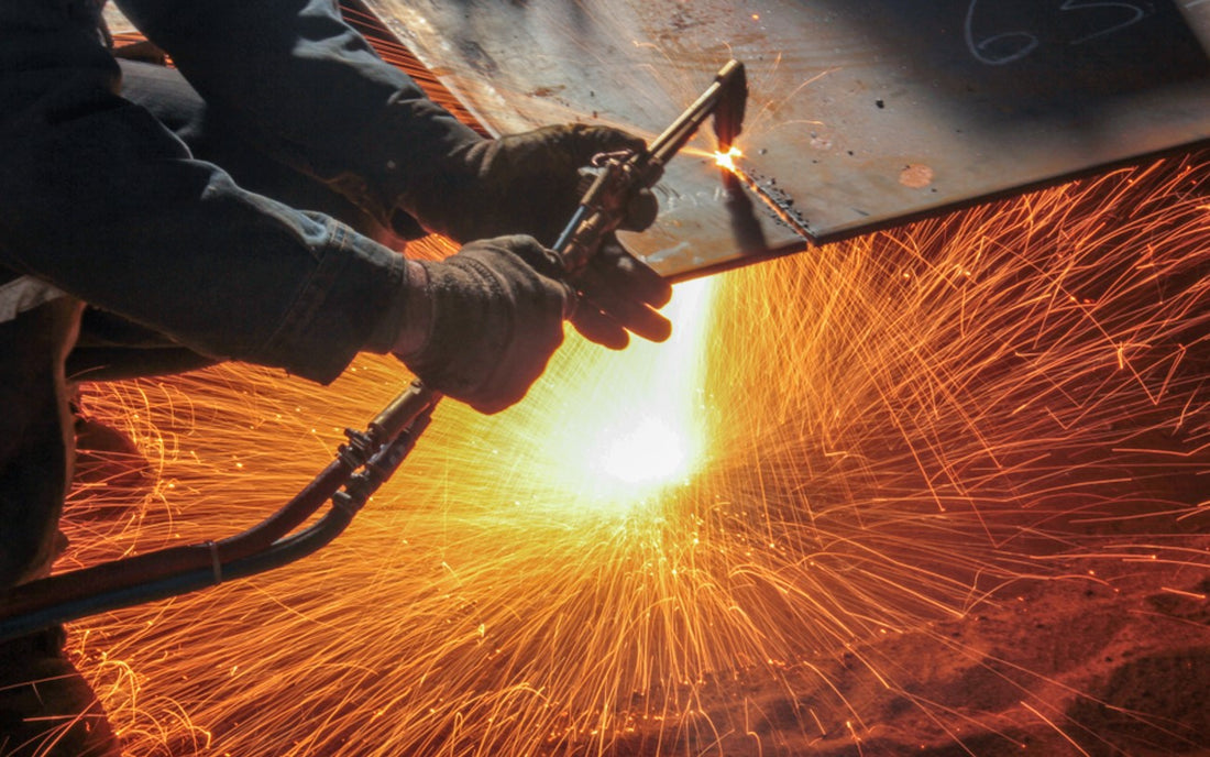 Welder wearing safety gloves using cutting torch with tip on metal sheet