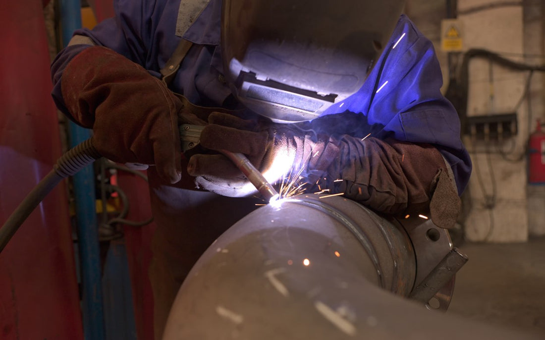 Worker welding metal pipe in industrial setting