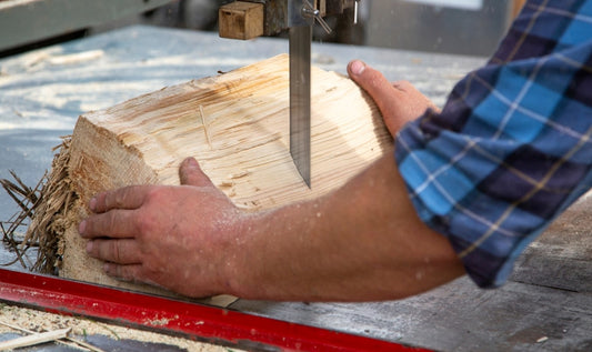 man holding a block of wood with two hands while a bandsaw blade cuts through it